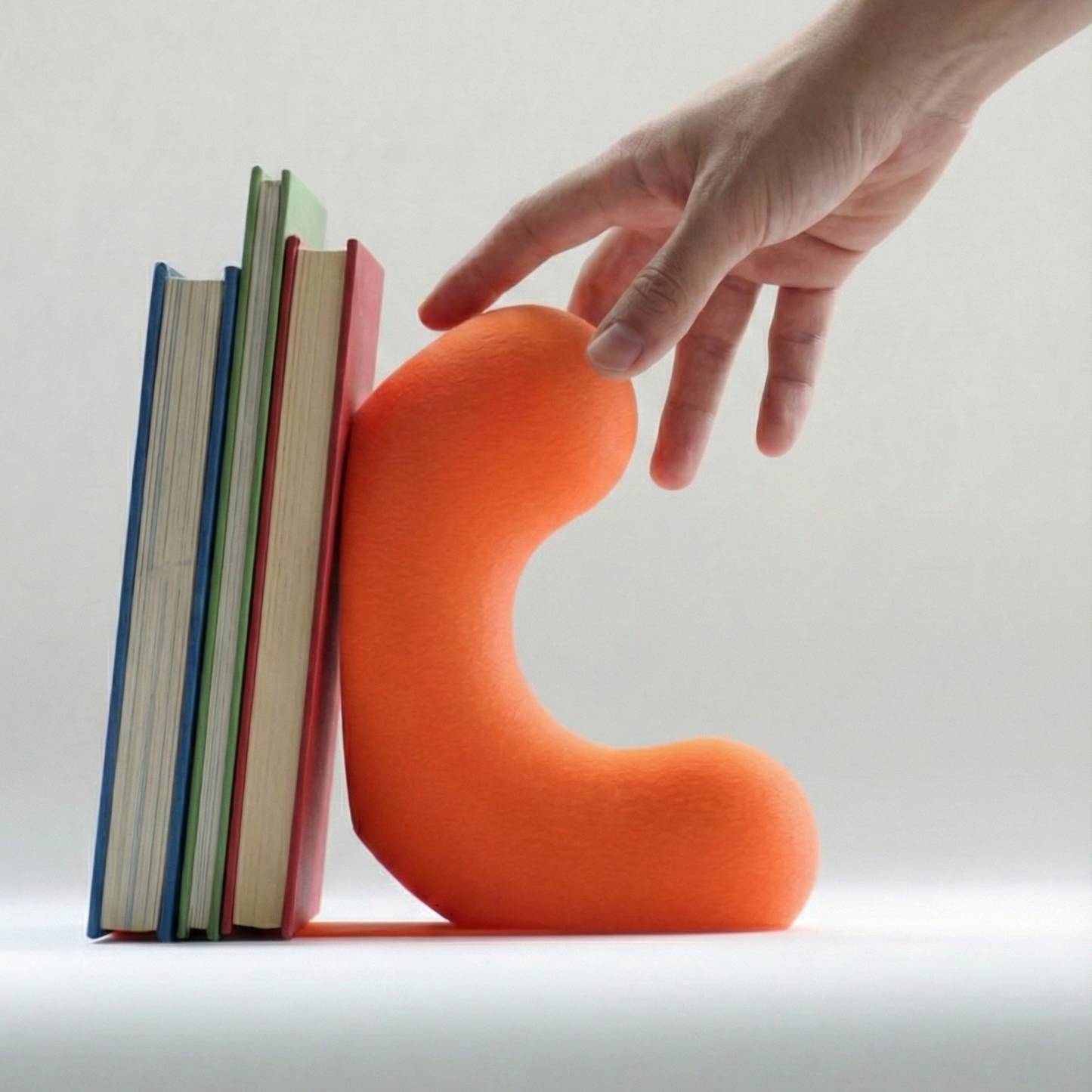 Présentation d'un serre livre orange et moderne tenant des livres pour enfant. Une main venant de la droite s'apprête à saisir le grand serre livres.  