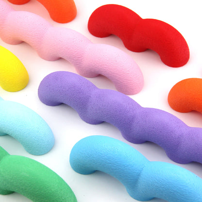Gros plan en angle sur quatre poignées de meubles en forme de vagues texturées (violet, rose, jaune et orange), disposées en diagonale sur un fond blanc uni. Leur fini mat et finement strié (suggérant l'impression 3D) met en valeur leur design ondulé unique.