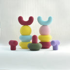 Une mise en scène studio sculpturale et ludique des crochets muraux colorés Benga Studio sur fond blanc. Au centre, plusieurs crochets mates sont empilés en équilibre à la manière d'un totem.  Cette composition artistique met en valeur le design pop et modulable de la collection.